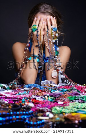 Young beautiful woman crying over heap  of  jewelry and bijouterie on black background
