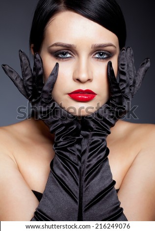 Young brunette woman with long black gloves posing on gray background
