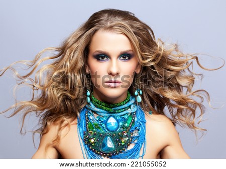 Portrait of beautiful young woman with bijouterie and fluttering hair on gray background