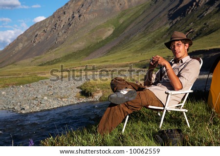 man sitting in the chair at the camp in mountains near the stream