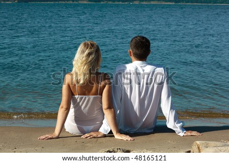 backview of romantic slavonic couple - blonde girl in peignoir and brown haired man in white shirt taking their time on the beach