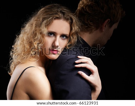 portrait of couple - blonde girl embraces man from behind. man's face in dark