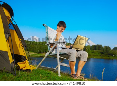 expression portrait of succesful man with laptop sitting in folding chair near camp tent outdoors
