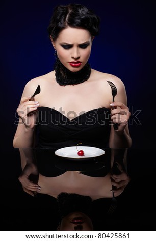 expression portrait of beautiful unhappy brunette girl with fork knife, and single red cherry on white plate