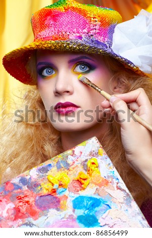 artist's hand with paintbrush painting beautiful girl's colorful eye shadow make up using palette