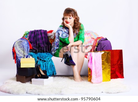 full-length portrait of young shopaholic woman sitting on sofa among clothes, boxes and shopping bags and looking at new court shoes