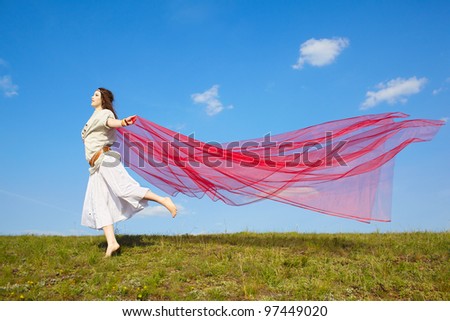 outdoor portrait of beautiful hippie girl running with big piece of red light cloth under the blue sky