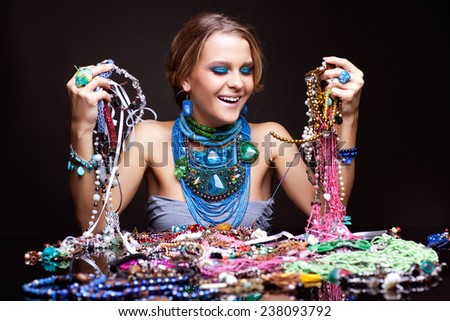 Laughing young beautiful woman over heap of bijouterie on the table with beads in hands