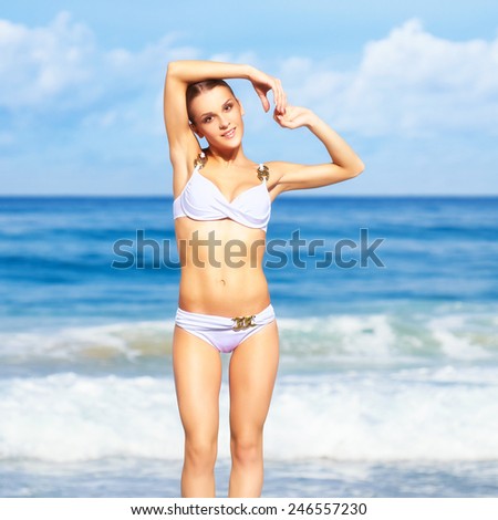 portrait of young beautiful slim woman in white bikini posing on sea background