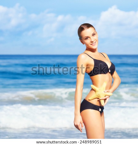 portrait of young beautiful woman in black bikini with sea-star on sea background