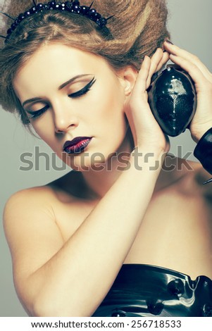Woman in dress and diadem made of molten vinyl disk with alien face in hands