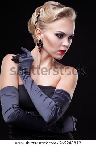 Young blonde woman in black dress and long gloves on dark background