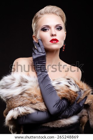 Young blonde woman in black dress and lynx fur with and long gloves on dark background