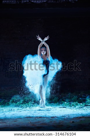 Young woman jumping in blue powder cloud on deserted factory grunge background