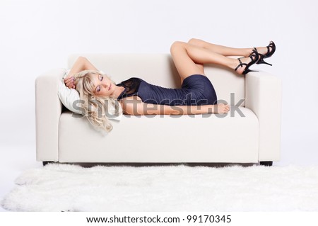 full-length portrait of beautiful young blond woman sleeping on couch with white furs on floor