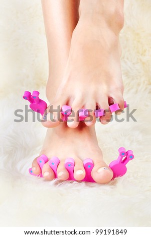 body part shot of beautiful healthy young woman\'s feet in pedicure toe separators on white fur