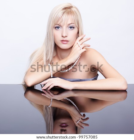portrait of young beautiful blonde woman sitting at mirror table with string of pearls