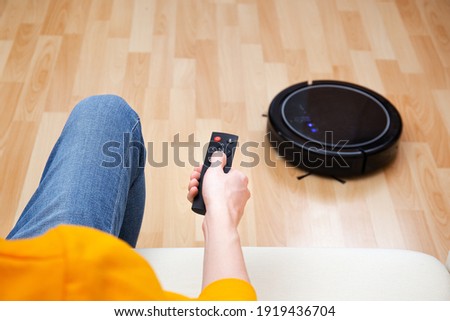 Man resting while robotic vacuum cleaner doing chores, clean work at home. Man controls a robot vacuum cleaner using a remote control. Cleaner robot vacuum cleaner cleans the floor