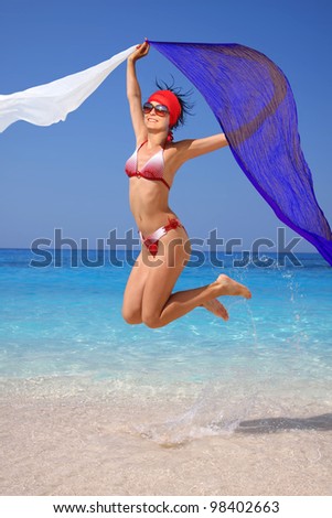 Sexy young Woman jumping on the beach with flying colorful scarf
