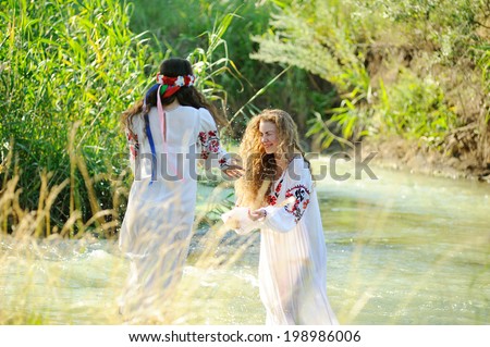 two girls in the Ukrainian national clothes swimming in the river. One girl splashes water on the other.