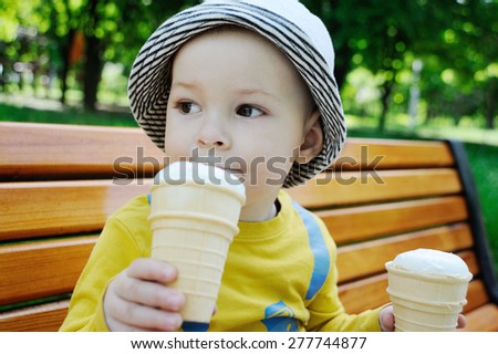a little boy holding two ice creams. baby gray panama eating ice cream