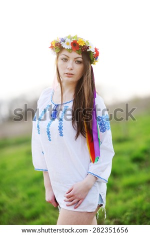 Ukrainian girl in a shirt and a wreath of flowers and ribbons on his head on a background of green grass