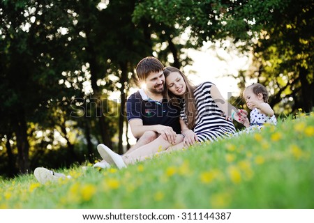 Young family on vacation in the park. mother, father and little daughter sit on the grass. Mother gives his daughter a small flower.