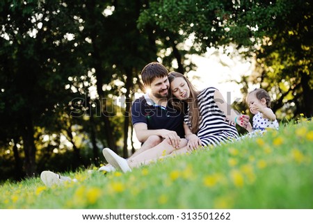 Young family on vacation in the park. mother, father and little daughter sit on the grass. Mother gives his daughter a small flower.