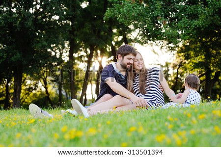 Young family on vacation in the park. mother, father and little daughter sit on the grass. Dad gives his daughter a small flower.