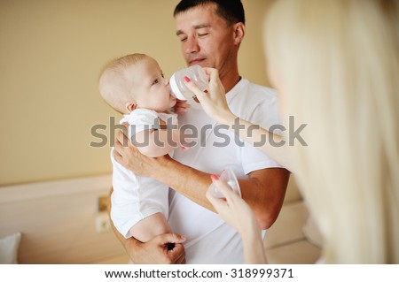 Dad holding a baby in her arms, mother feeds her baby son bottle milk formula