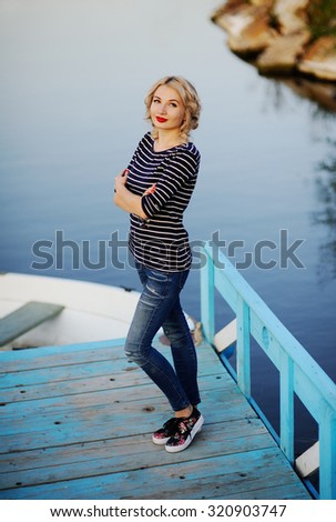 girl in a striped blouse standing on a wooden bridge on a background of the river