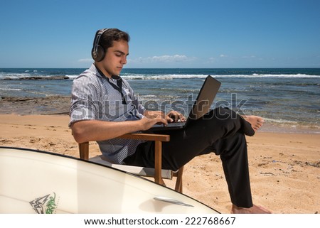 Horizontal photographic image of young man with computer and surfboard on sunny beach in Australia