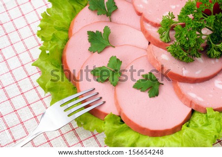 Slices of sausage with greenery on the plate and a fork