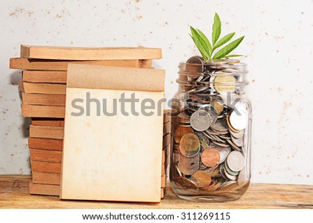 Old Book and Money with growing sprout in glass jar on wooden table