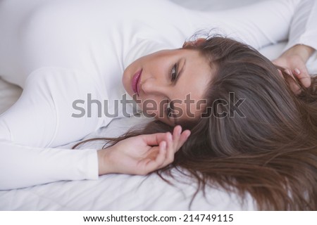 Woman in underwear is lying in the bed with white bed linen, white background
