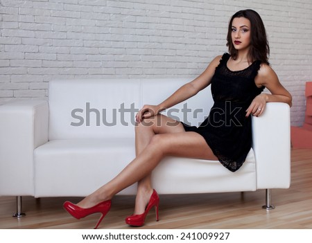 Portrait of beautiful and attractive young adult sensuality and sexy female brunette woman posing in  black dress on the sofa