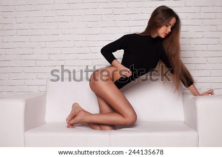 Portrait of beautiful and attractive young adult sensuality and sexy female brunette woman posing in black bikini on the sofa