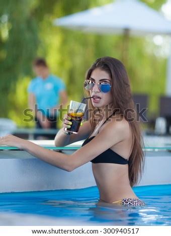 beautiful woman in orange bikini and sunlasses sitting in swimming pool with cocktail. Fashionable portrait. Elegant woman in a bikini.