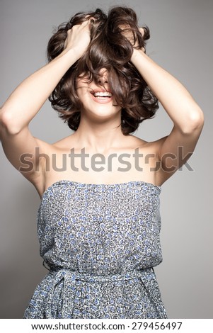 Awesome caucasian attractive joyful happy sexy female model is shaking head with brunette hair in studio wearing nice dress, isolated on gray background