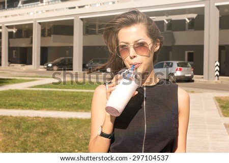 Young attractive female fashion mode wearing fashionable dress drinking dietary cold fruit smoothie milk shake in the city while the weather is too hot