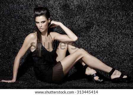 sexy fashion model with natural brunette hair, long legs, full lips, perfect skin, wearing black shoes and transparent cocktail dress, sitting on black carpet, beauty photoshoot, retouched image