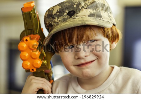 4 year old boy wearing his mother\'s old Army ACU cap while holding a toy laser gun--image taken indoors using natural light (Reno, Nevada, USA)