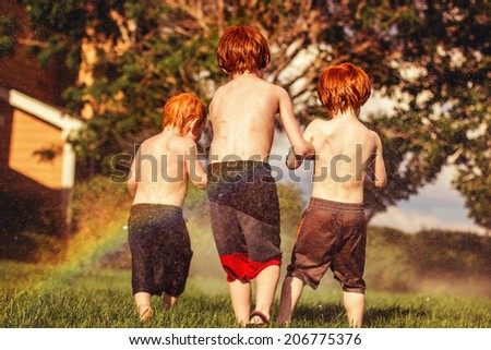 Three young brothers playing in the sprinklers on a hot day -- image taken outdoors in Reno, Nevada, USA