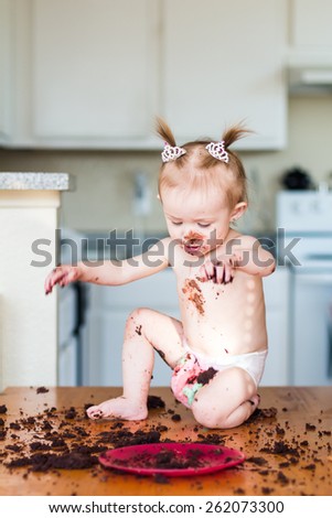Baby girl with pigtails celebrating her first birthday with a chocolate cake. Photo taken in a home in Reno, Nevada, USA with natural window light.