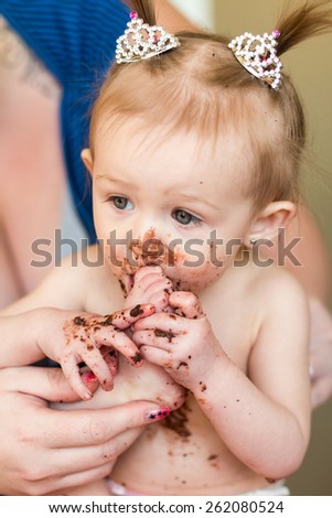 Baby girl with pigtails celebrating her first birthday with a messy chocolate cake. Photos taken inside a home in Reno, Nevada, USA using natural window.
