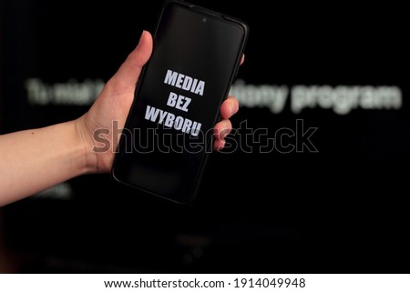 Media blackout protest in Poland. A person is holding a smartphone with the sign “Media bez wyboru” (Eng. Media without a choice) in front of a black TV screen. Imagine de stoc © 