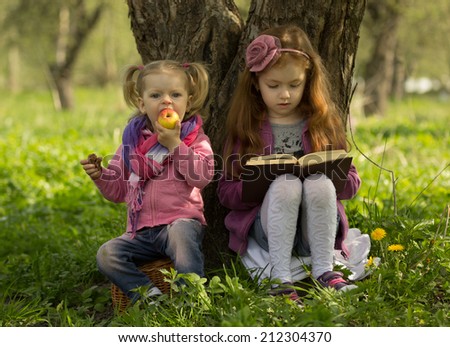 one little girl reads book and other little girl eats apple