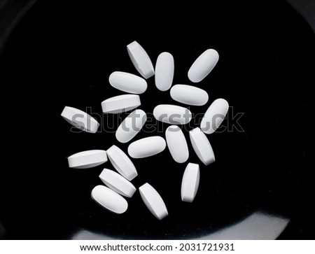 Several vitamin tablets on a black ceramic dish, close-up, top view. Stock fotó © 