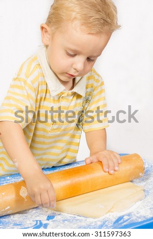 Boy knead the dough by plunger for making a cake on a blue tablecloth