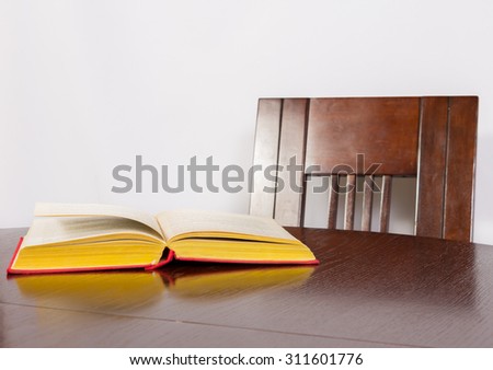 Book with a red cover lies on brown wooden table on a white background